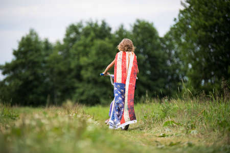 Symbol of celebration 4 fourth of july. Young Girl riding bicycle with american flag in handの写真素材
