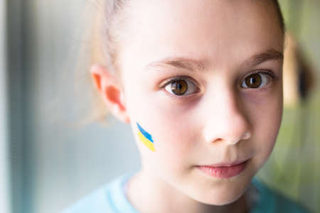 face of a frightened girl, a painted heart on the cheek in yellow-blue colors of the Ukrainian flag.の写真素材