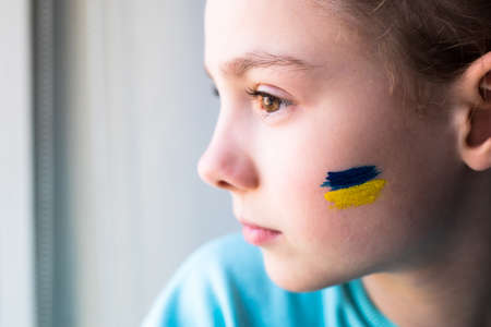 face of a frightened girl, a painted heart on the cheek in yellow-blue colors of the Ukrainian flag.の写真素材