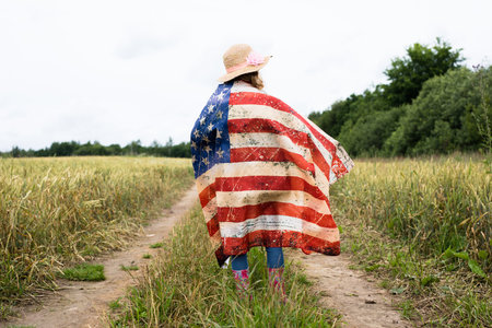 Person wrapped in American flag standing on a dirt path in a field