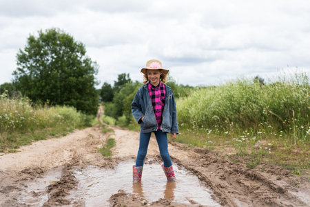 Standing in a puddle on a country path while wearing boots and a hatの写真素材