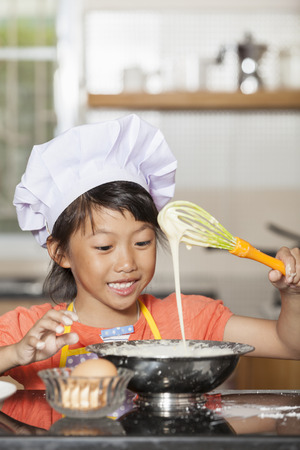 Little asian girls stiring wheat flour and eggの写真素材