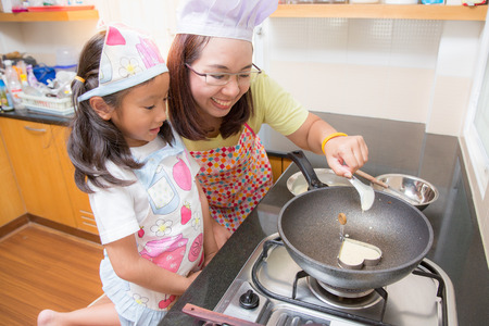 Asian family enjoy making pancake, Asian mother and daughter enjoy making bakery cake, Little Asian girl and mom enjoy decorate cake in real life kitchen,Asian mom teaching daughter to learn making pancake in real life kitchen at homeの写真素材