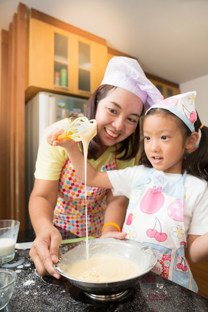 Asian family enjoy making pancake, Asian mother and daughter enjoy making bakery cake, Little Asian girl and mom enjoy decorate cake in real life kitchen,Asian mom teaching daughter to learn making pancake in real life kitchen at homeの写真素材