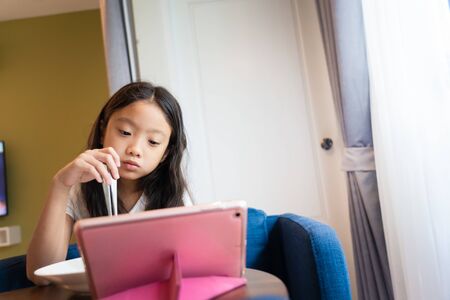 Little Asian girl watching internet content in computer tablet during eating