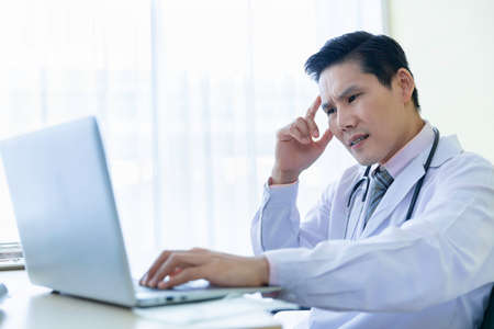Stress headache male asian doctor working in clinic office at hospital