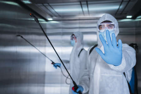 Man in virus protective suite and mask spraying alcohol cleaning covid19 infected area, Virus disinfection conceptの写真素材