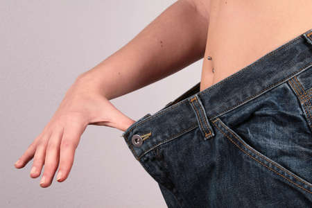 The New Me! - woman showing how much she has lost by putting on an old pair of jeans.の写真素材