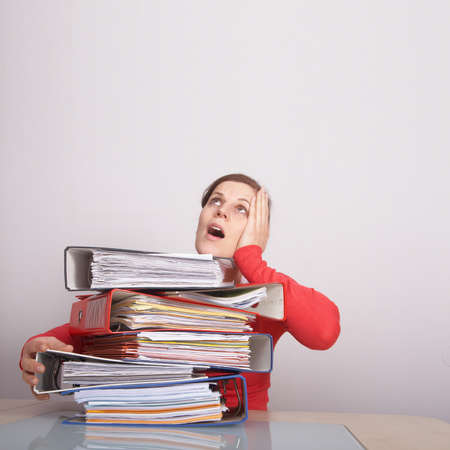 A young and beautiful female student is stressed with a lot of paperwork in front of her. A lot of...