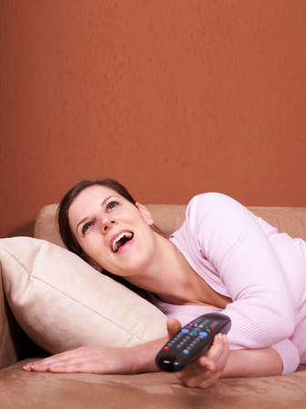 A young woman sits in front of a TV with the remote control in her hand on a couch. A lot of...