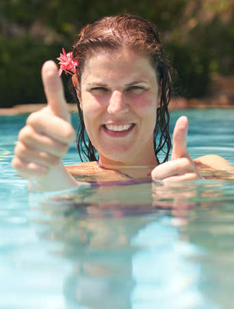 Young woman in a beautiful pool with palms in the background. She is showing a thumbs up sign.