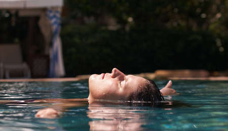 Young woman in a beautiful pool with palms in the background.の写真素材