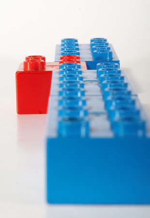 Building bricks in blue and one red block being unique and standing out. Over white background with shadows to show depth. Focus is on the block standing out.の写真素材