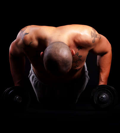 Young bald strong man is working out over black background.