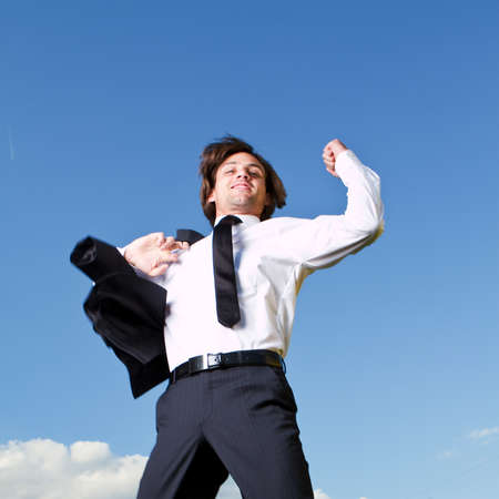 Young busiinessman is jumping with joy over a blue sky in a garden.の写真素材