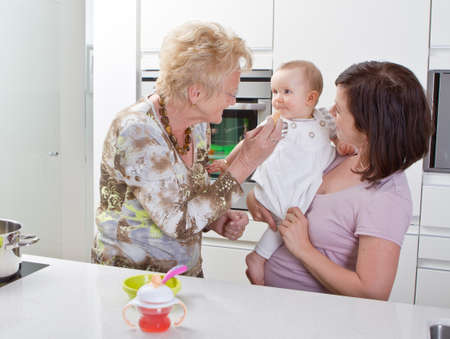 Young mother with baby girl and the grandmother in a modern kitchen setting.