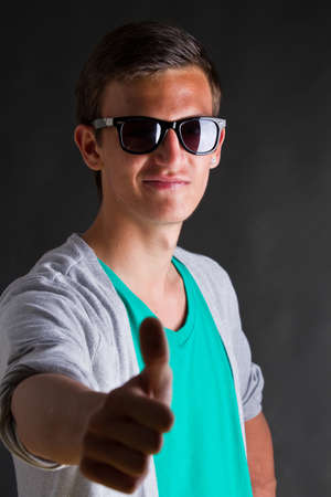 Thumbs up sign - given by a young man with cool sunglasses and a green shirt.の写真素材