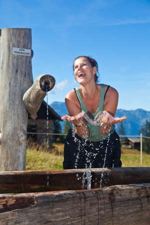 Young woman drinking water and splashing in joy after a long hike.の写真素材