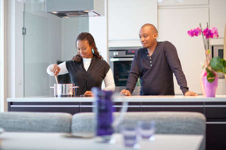 Colored couple in a modern kitchen setting. The woman is cooking.の写真素材
