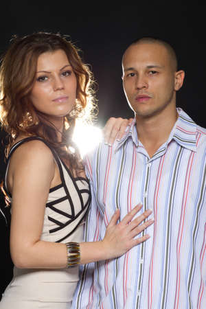 Young interracial cute looking couple over black background.