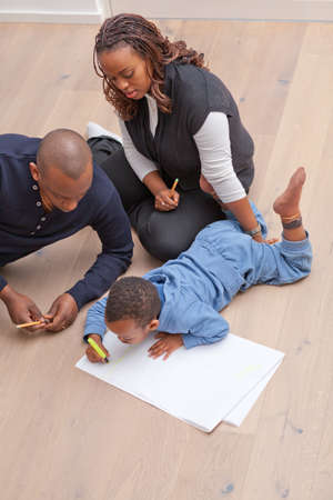 Young black family sitting on the floor drawing a picture with their son の写真素材