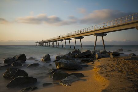 a long pier above the sea illuminated by the early morning sunの写真素材