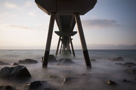 a long pier above the sea illuminated by the early morning sunの写真素材