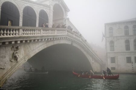 Rialto Bridge In Venice surrounded by fog with a gondola passing under itのeditorial素材