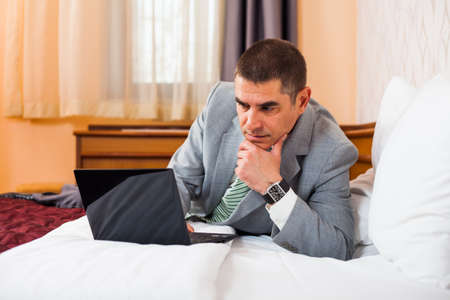Businessman is lying in bed and working on laptopの写真素材