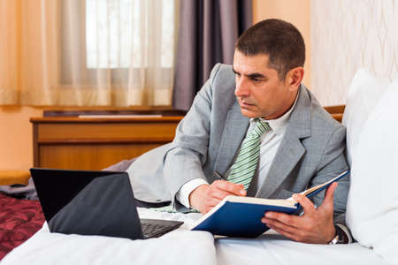 Businessman is lying in bed and workingの写真素材