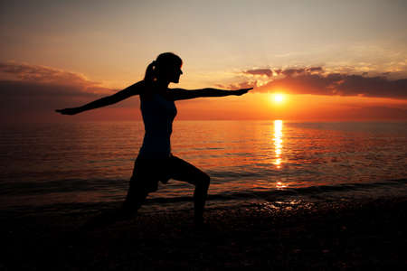 Silhouette of girl meditating on the beach in sunsetの写真素材