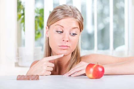 Woman looking at apple and candy, fruit or candy dilemmaの写真素材