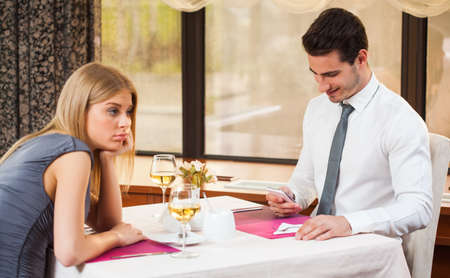 Woman is getting bored in restaurant while her boyfriend is typing smsの写真素材