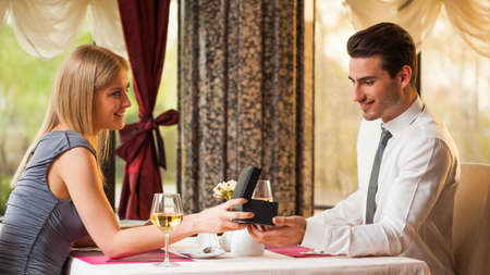 Happy couple at restaurant, girlfriend is giving present to her boyfriendの写真素材