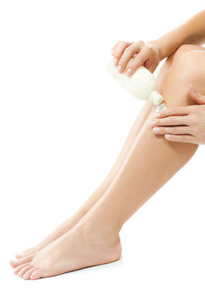 Young woman putting skin cream on her leg, isolated on whiteの写真素材