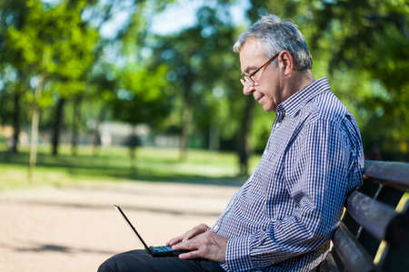Senior man using laptop in parkの写真素材