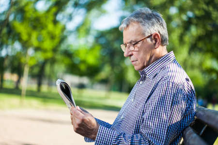 Portrait of senior man reading newspaper in parkの写真素材