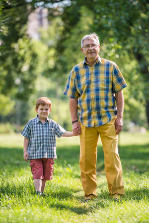 Grandfather and grandson walking in parkの写真素材
