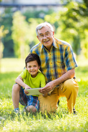 Grandfather and grandson using digital tablet in parkの写真素材