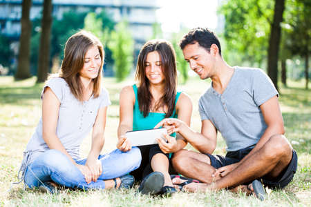 Happy friends using digital tablet in park on a summer dayの写真素材