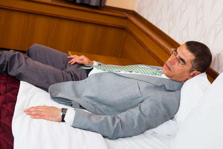 Tired businessman is sleeping on bed in hotel roomの写真素材