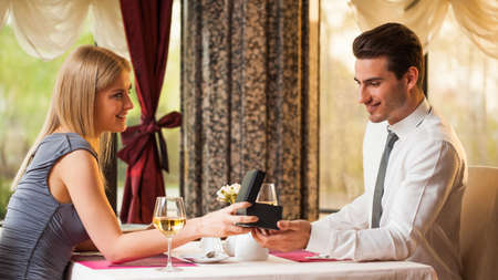 Happy couple at the restaurant, girl is giving present to her boyfriendの写真素材