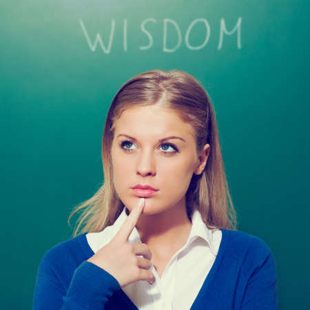 Young teacher thinking in front of blackboard, intentionally toned.
