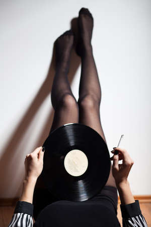Woman lying on floor, holding vinyl record and smoking cigaretteの写真素材