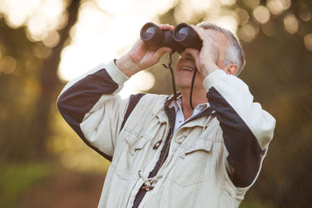 Senior man looking through binoculars in parkの写真素材