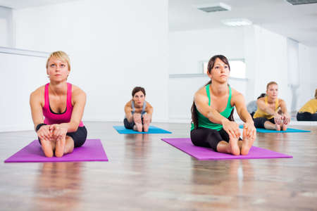Four girls practicing yoga, Pascimottanasana Seated Forward Bend pose