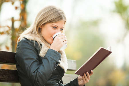 Young woman reading book and drinking coffee to goの写真素材