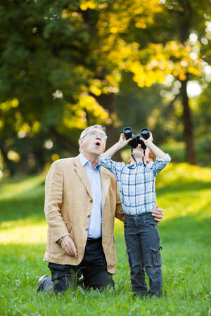 Grandfather and grandson watching nature with binoculars in parkの写真素材