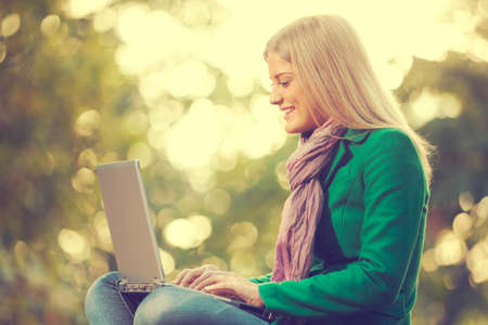 Happy woman using laptop in park, intentionally toned.の写真素材