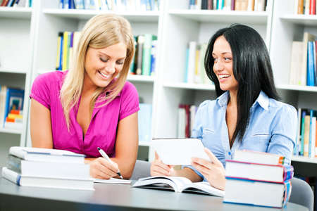 Two happy student girls learning in library, using digital tablet.の写真素材